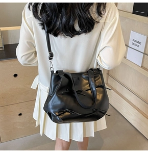 Detail of black PU leather handbag featuring four matching bows on a smooth surface