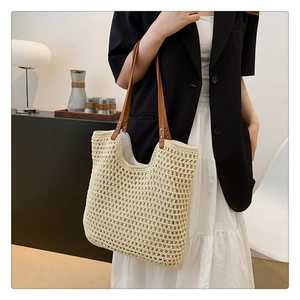 Detail of hollow knit tote bag with brown leather straps and metal rivets on beige texture