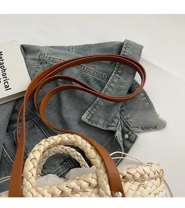 Close-up of straw woven handbag with brown leather strap on denim jacket background