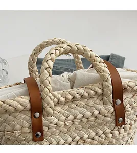 Detailed close-up of the woven straw tote bag handle with leather accents and metal rivets