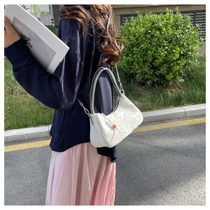 Detail shot of white butterfly print crossbody bag with red bead charm in outdoor light