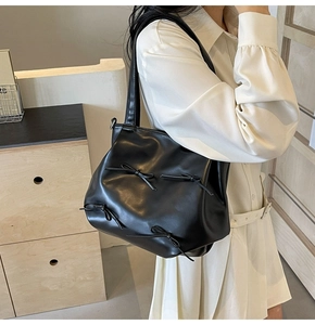 Detail view of black PU leather crossbody bag with decorative bows on a model