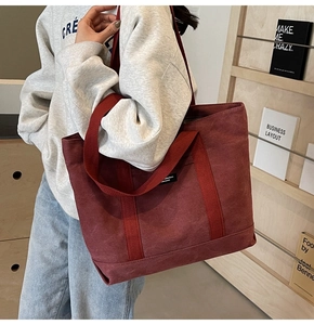 Close-up of a burgundy canvas tote bag with woven handles in a minimalist indoor setting