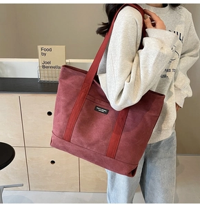 Burgundy canvas tote bag with black label and wide strap worn in a lifestyle setting