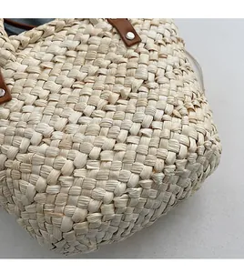Detailed close-up of woven straw fabric texture with leather handles and silver metal rivets