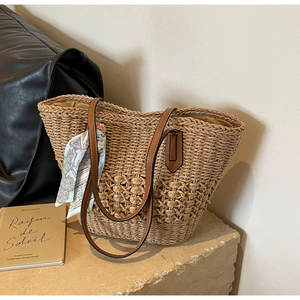 Minimalist straw woven tote bag with brown faux leather handles and decorative silk scarf
