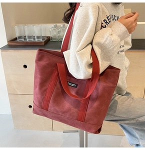 Detail of a dark red canvas tote bag with black logo patch and wide shoulder strap