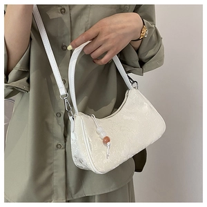 On-body view of white embossed texture handbag with beaded charm and long strap