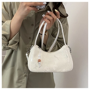 Detail of white crescent bag showing floral texture, silver hardware and bead charm