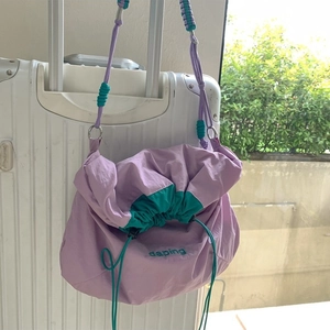 Sac bandoulière en nylon violet et bleu sarcelle avec cordon suspendu à une valise