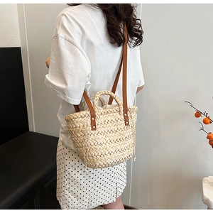 Detail view of woven straw bag featuring brown leather strap and white drawstring lining