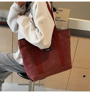 Detail view of the burgundy canvas tote bag worn by a model in a minimalist room