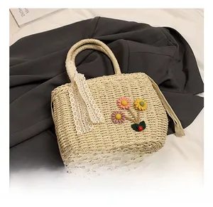 Vue détaillée d'un sac à main en paille beige avec fleurs artisanales et ruban de dentelle