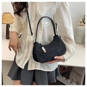 Detail of black floral jacquard hobo bag with beaded charm and leather strap on model