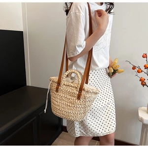 Detail view of woven straw tote bag with brown leather handles and silver rivet accents