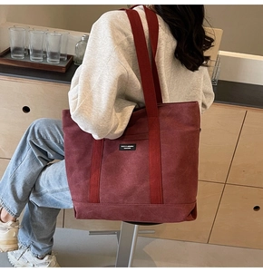 Detail of burgundy canvas tote bag showing wide shoulder straps and square logo tag
