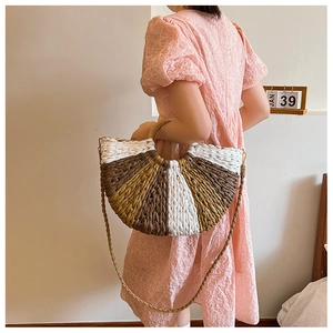 Detail view of a semi-circular striped straw handbag worn by model in a chic indoor setting