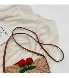 Detail of straw woven bucket bag featuring 3D red cherry accents and a slim leather strap