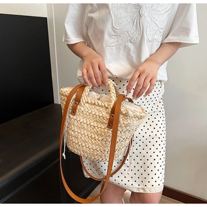 Detail of straw woven bucket bag featuring brown leather shoulder strap and drawstring liner