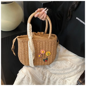 Détail d'un sac en paille tressée avec fleurs au crochet et ruban en dentelle sur l'anse