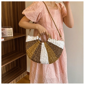 Detailed close-up of a semi-circular straw bag with woven top handles and a pink dress backdrop