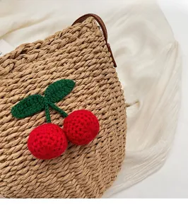 Close-up of hand-woven straw bucket bag with red cherry crochet and brown leather strap