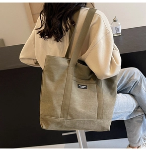 Olive green canvas tote bag with wide straps and external pocket shown on shoulder