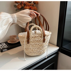 Close-up of straw woven tote bag with brown leather strap and drawstring lining