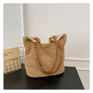 Minimalist beige knitted tote bag with brown leather handles on a dark table