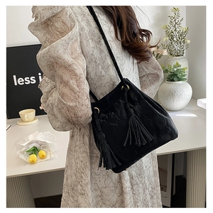 Détail du sac bandoulière noir avec texture plissée et glands à franges sur modèle