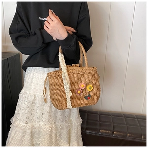 Détail du sac à main en paille avec fleurs colorées et rubans en dentelle blanche