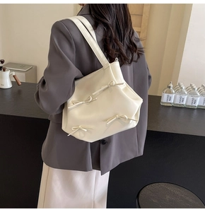 Detail of cream white PU leather crossbody bag with four decorative bows on a model
