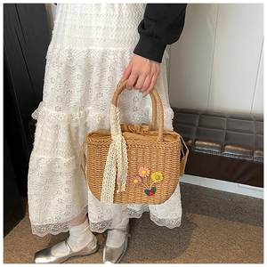 Détail du sac en paille tissée avec fleurs en tricot, rubans en dentelle et cordon