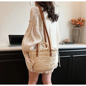 Detailed close-up of straw woven tote bag featuring brown leather handles and side drawstring