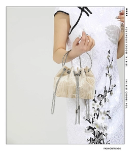 Close-up of champagne velvet pleated bucket bag with chain strap and tassel drawstring
