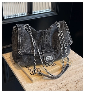 Close-up of denim crossbody bag with silver rotating lock and metal chain strap