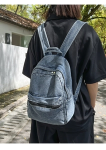 Detailed back view of a vintage washed blue denim backpack worn by a model in nature