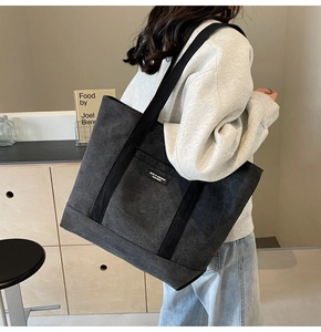 Detail view of a black canvas tote bag with wide shoulder strap on a female model