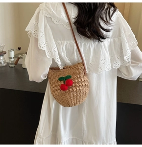 Detail of straw bucket bag with hand-woven cherry accents on a white lace dress