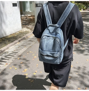 Close-up of light blue washed denim backpack with silver zippers and multi-pocket detail