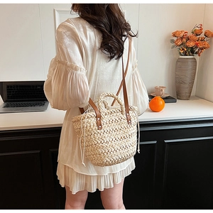 Detail of a straw bucket bag with white drawstring and brown leather strap on a table