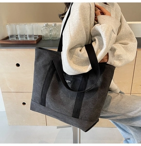 Detailed view of a spacious black canvas tote bag being worn in a minimalist studio setting