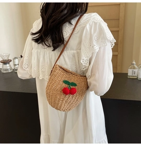 Detail of hand-woven straw bucket bag featuring red knit cherry charms and slim strap