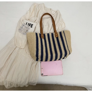 Detail of navy blue and beige striped straw tote bag with brown leather handles and rivets