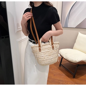 Straw woven tote bag with brown leather straps shown held by a model in a casual setting