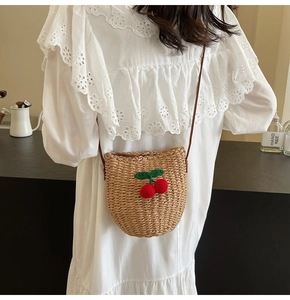 Detail of woven straw bucket bag featuring 3D red cherry accents worn with a lace dress