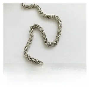 Close-up detail of silver braided metal chain strap on a white fabric bag surface