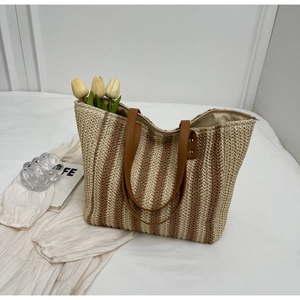 Detailed shot of striped straw tote bag with brown leather handles on white fabric