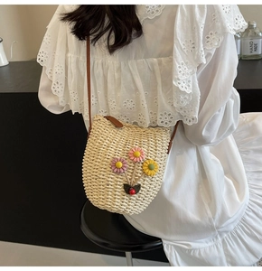 Detail of woven straw bucket bag with knitted flowers and brown leather strap