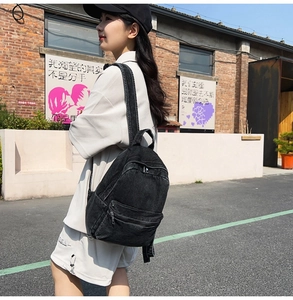 Detail view of washed black denim backpack with adjustable straps on a model back